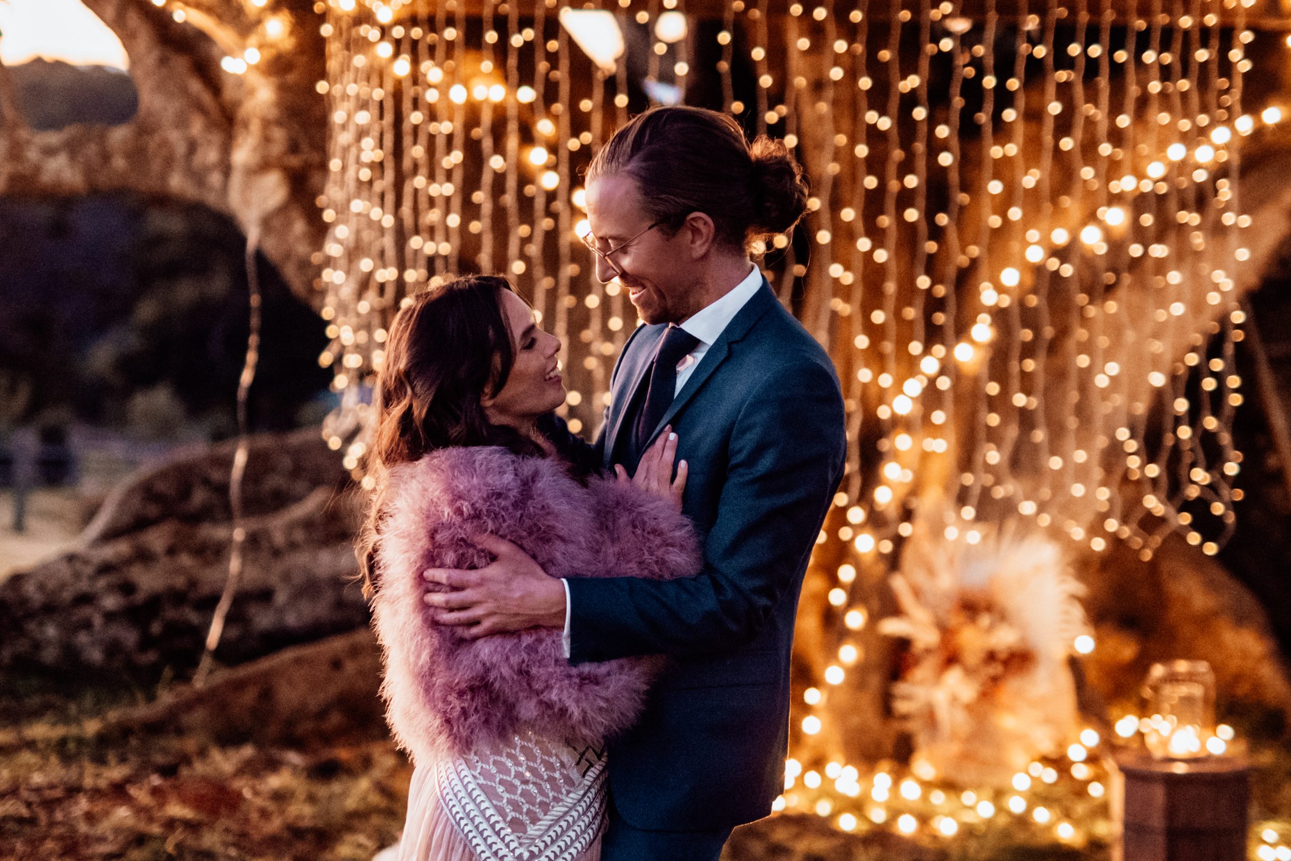 Bride and groom in winter stand in front of figtree with fairy lights after their wedding