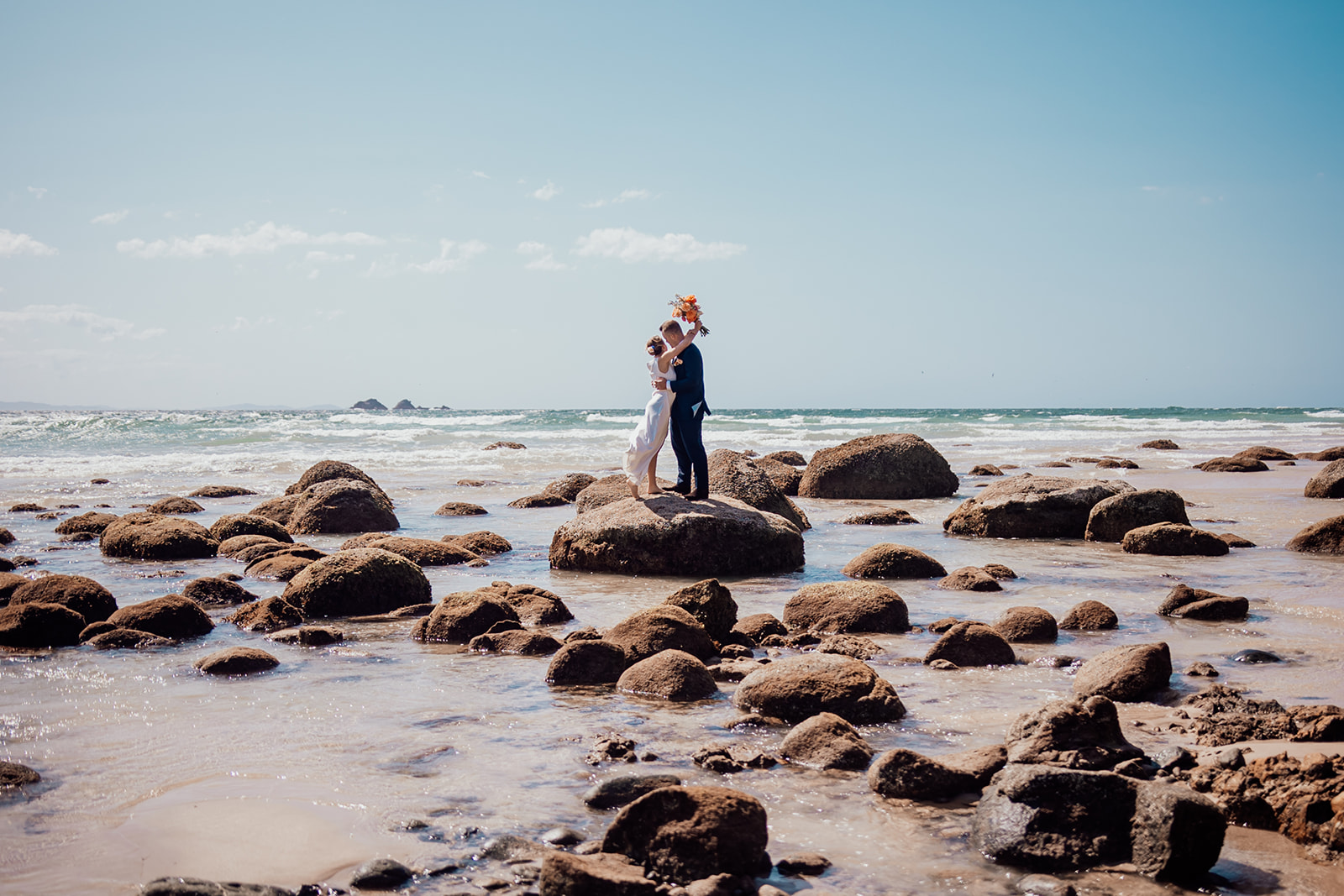 Bride and groom share first kiss on a rock at wategos beach, Byron Bay