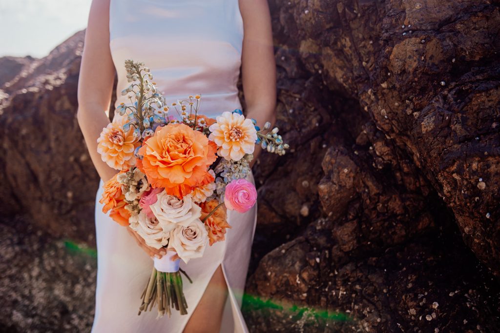 Bride holds bouquet set against rock backdrop at Wategos beach byron bay