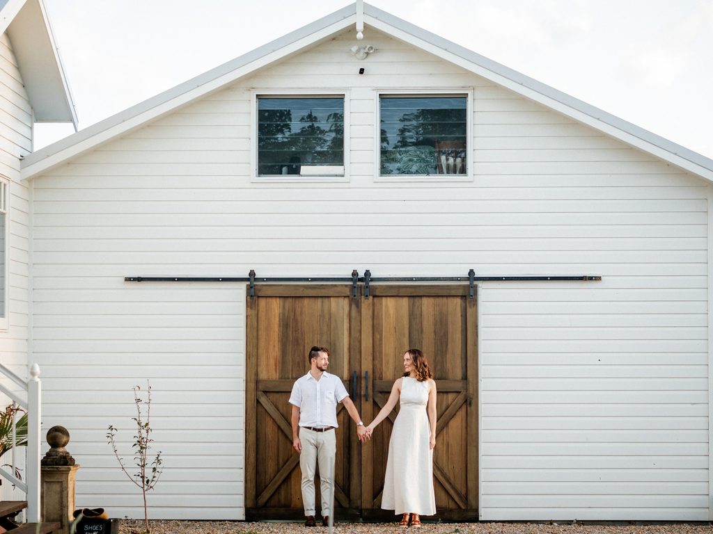 Cost and Inclusions wedding venue Byron Bay. A couple poses hand in hand in front of a barn door at Aurora House