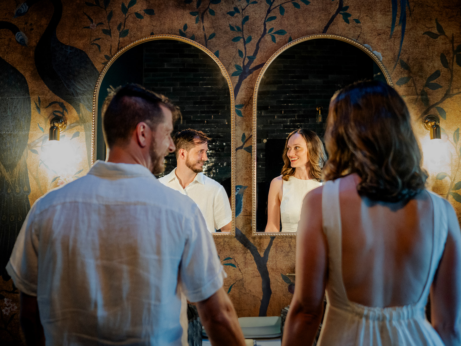 a couple look at each other and are reflected in two bathroom mirrors at Aurora House for their engagement shoot