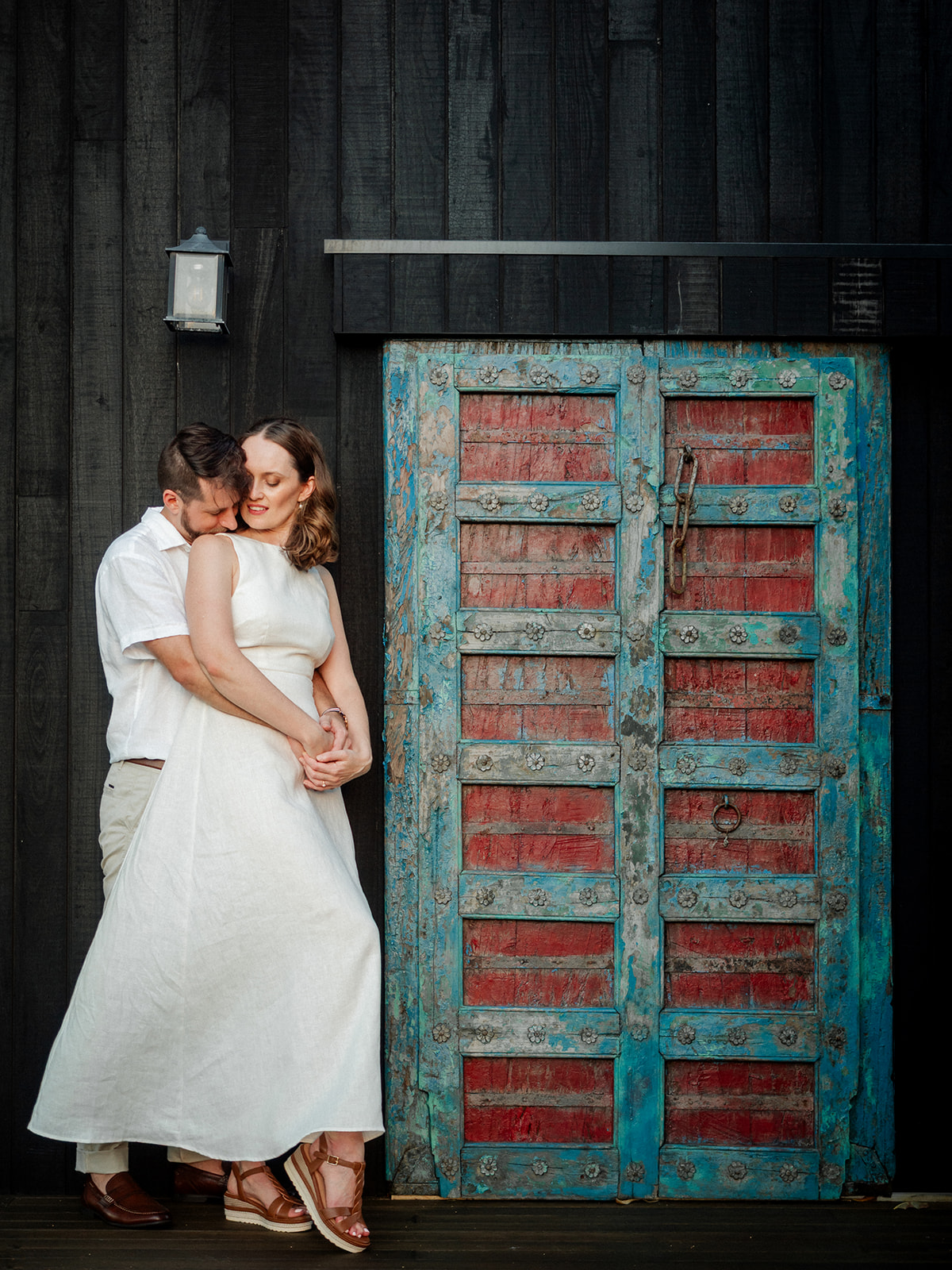 Byron Bay wedding venue- An engaged couple pose in front of a red and green Bali sliding door feature at Aurora house
