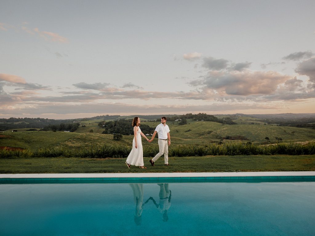 Northern Rivers wedding Venue. A couple walk hand in hand next to a pool overlooking byron Bay hinterland